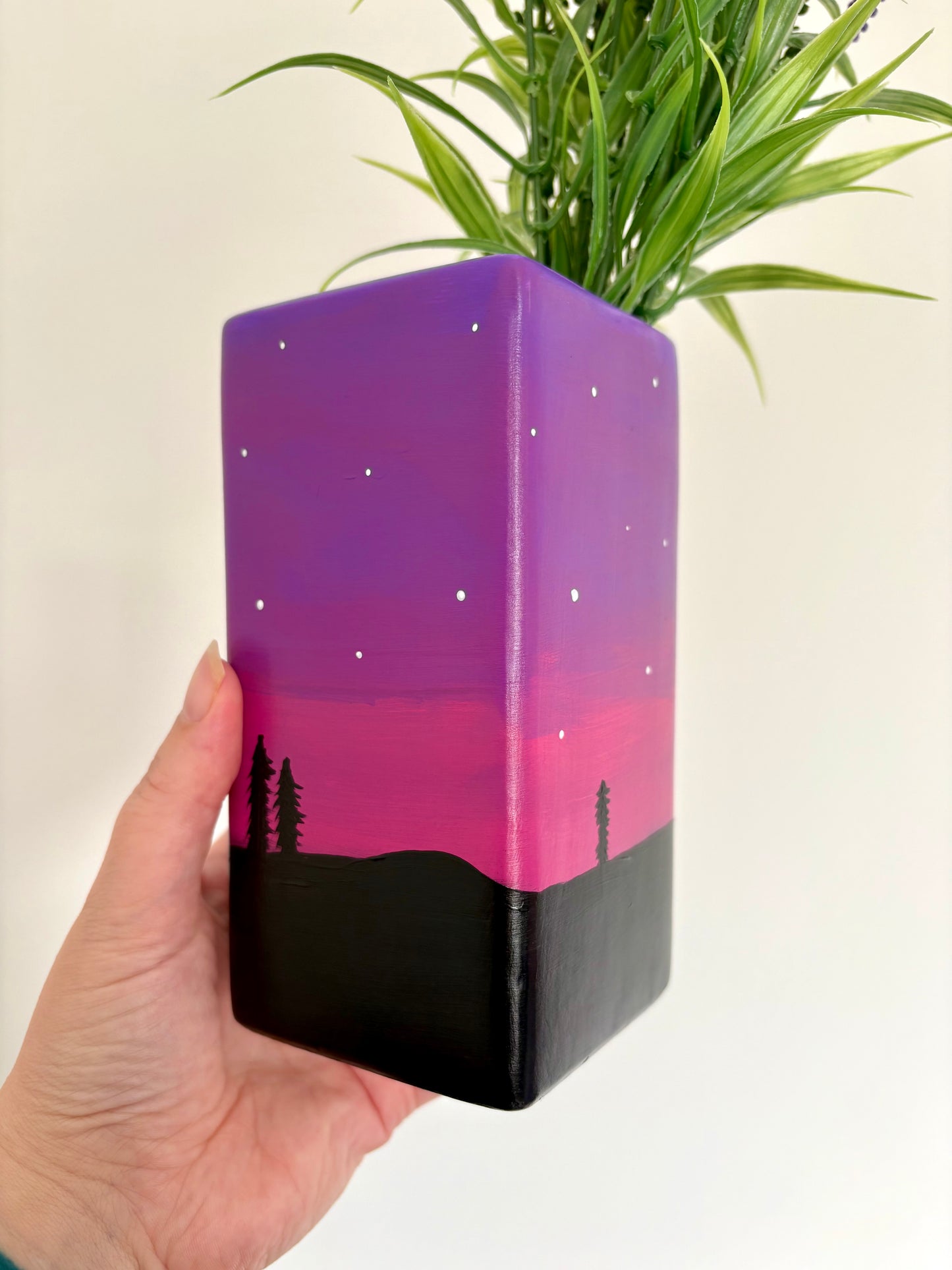 A square ceramic vase showing a hand painted night sky design featuring a purple and pink gradient, white stars, and a black tree silhouette