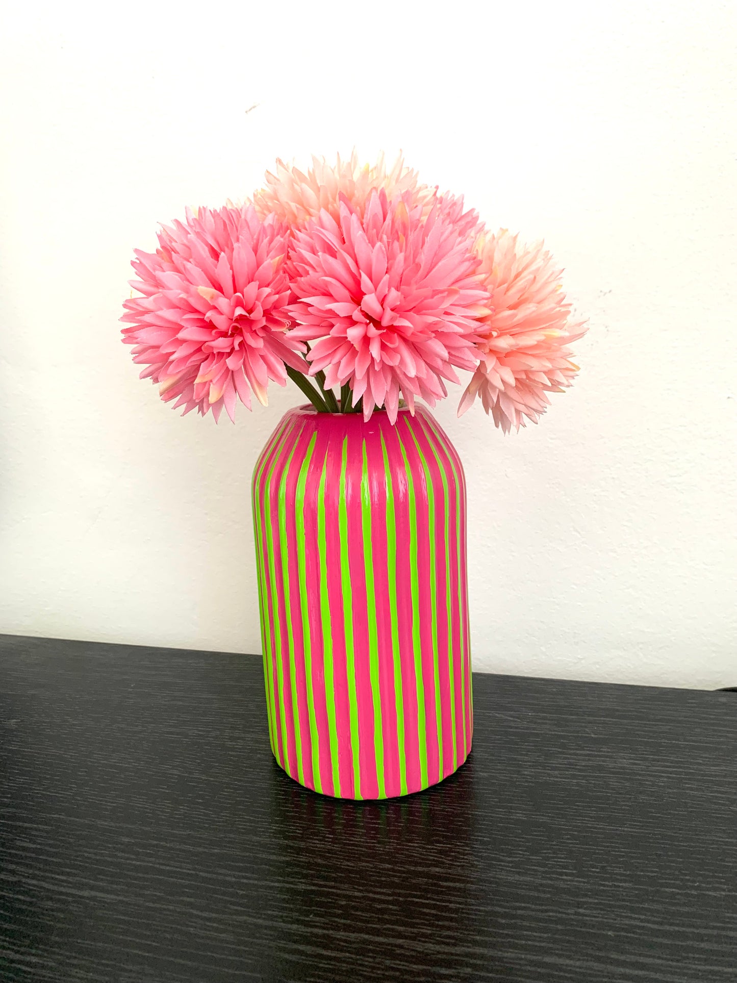 Green and fuchsia striped vase with pink flowers on a dark surface