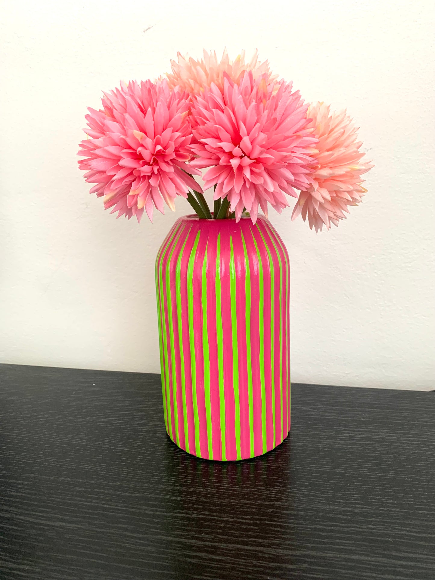 Green and fuchsia striped vase with pink flowers on a dark surface