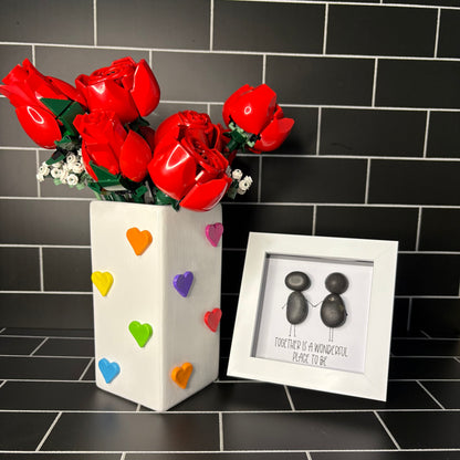 A hand painted white vase with hand crafted air dried clay rainbow hearts, accompanied by a small pebble art frame containing the phrase 'Together Is A Wonderful Place To Be'
