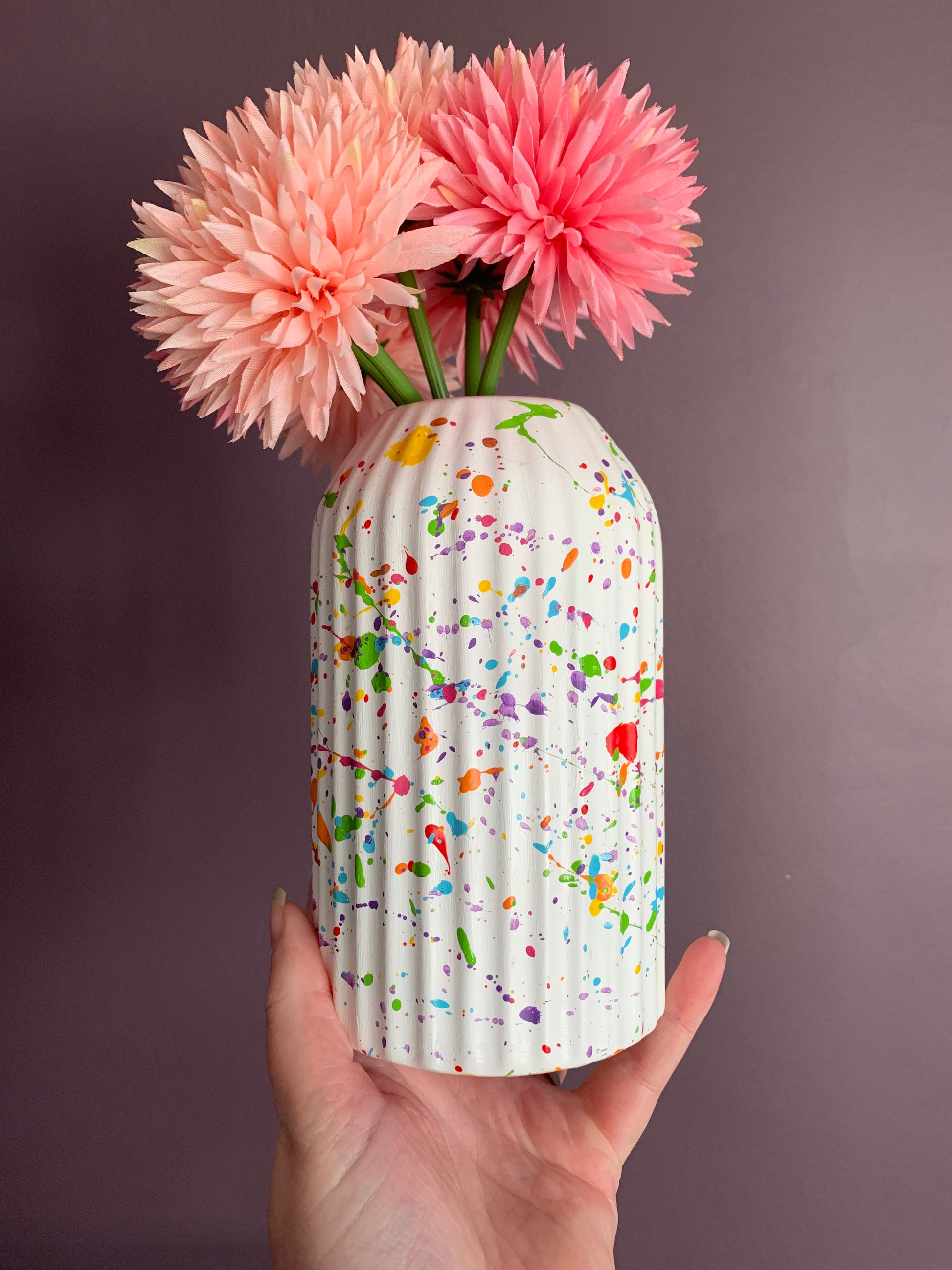 A white based vase with rainbow paint splat all over 