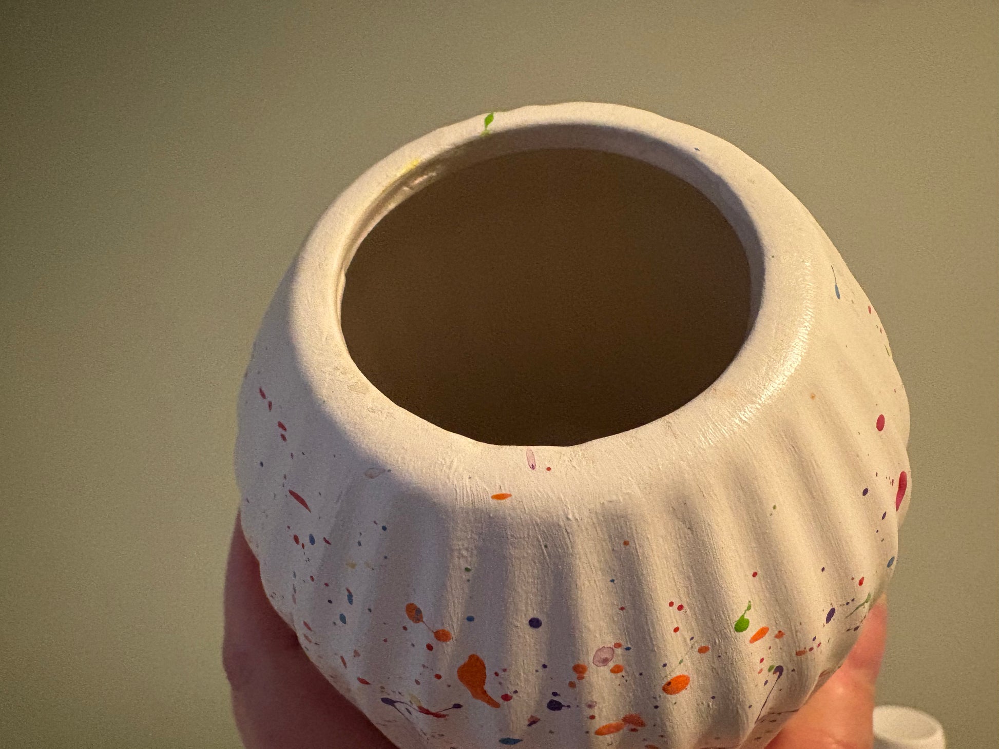 A ceramic vase splattered with rainbow paint, showing the slight blemishes at the top 