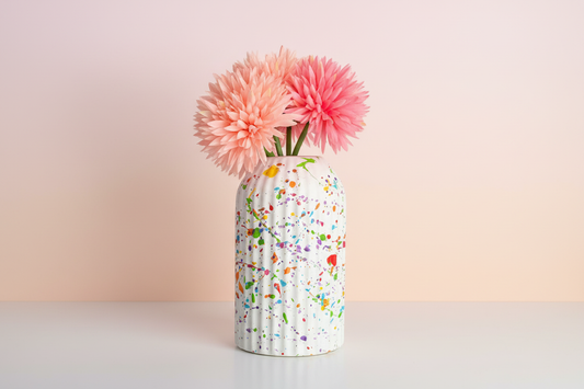 A ceramic vase splattered with rainbow paint 